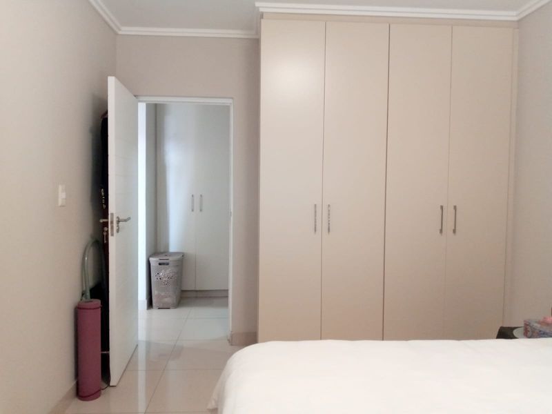 A well-maintained bedroom featuring neutral walls, tiled flooring, and ample built-in cupboard storage, with an adjoining room visible through the doorway.