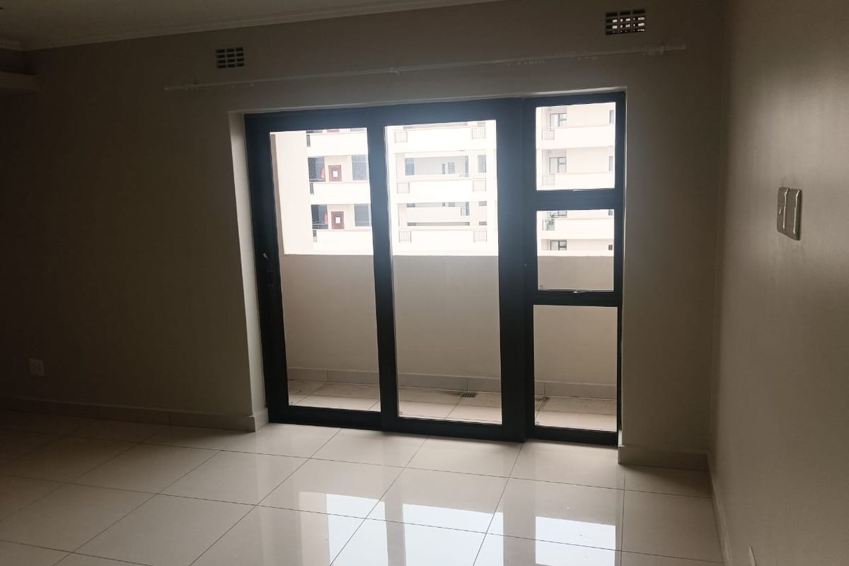An empty, well-maintained living area featuring neutral tiled flooring and a large sliding glass door providing access to an outdoor balcony.