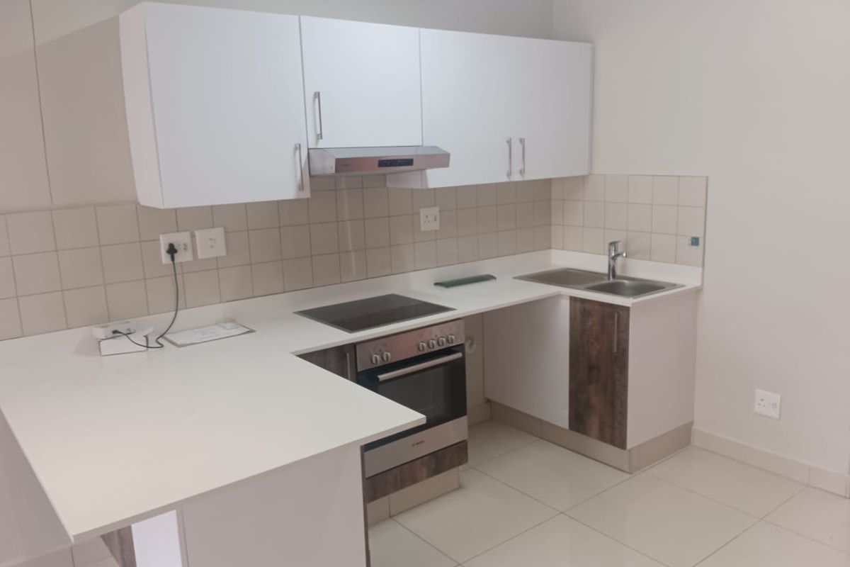 A clean, modern kitchen featuring white cabinetry, a built-in oven with electric hob, extractor fan, and a double sink with tiled backsplash.