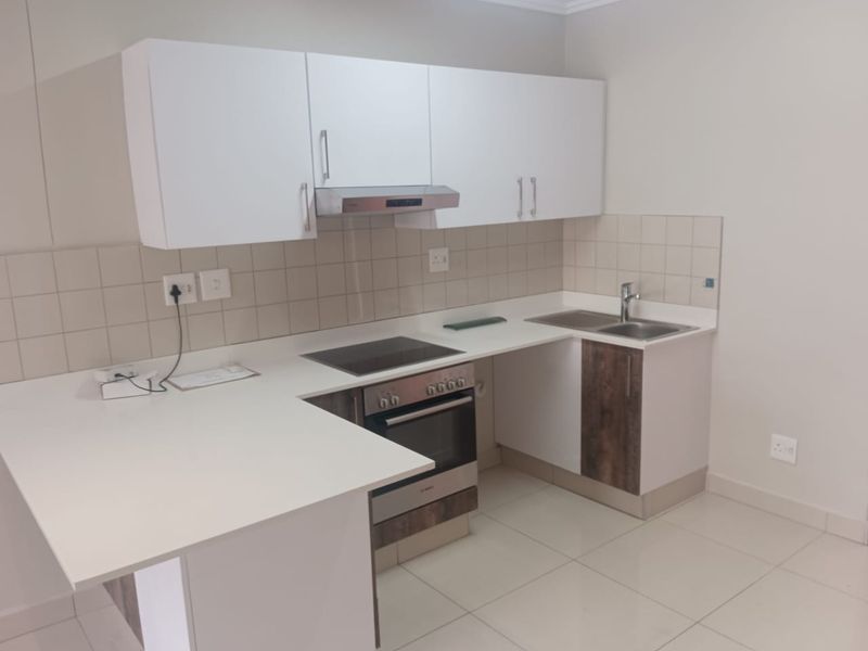 A clean, modern kitchen featuring white cabinetry, a built-in oven with electric hob, extractor fan, and a double sink with tiled backsplash.