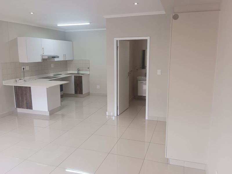 Open-plan kitchen featuring modern cabinetry and tiled flooring, leading into a bright living area with an adjacent bathroom entrance.