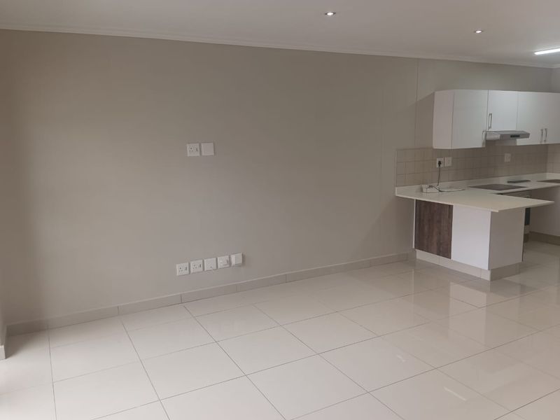 An open-plan living area featuring neutral tiled flooring, recessed lighting, and a modern kitchen with built-in cabinetry and integrated appliances.