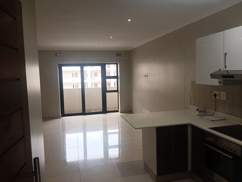 An open-plan living and kitchen area featuring modern cabinetry, built-in appliances, tiled flooring, and a large sliding door leading to a balcony.