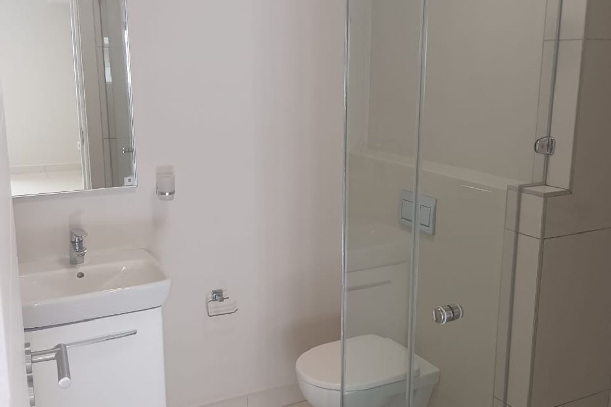 Modern bathroom featuring a wall-mounted vanity, wall-hung toilet, and a glass-enclosed shower with neutral tiled finishes.