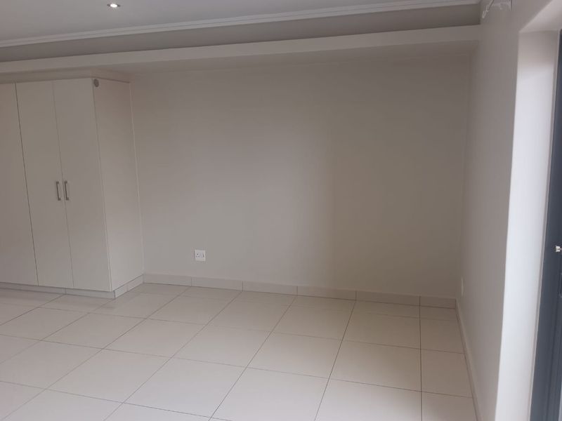 A clean, empty bedroom featuring neutral tiled flooring, built-in cupboards, and recessed ceiling lighting, providing a blank canvas for personalization.