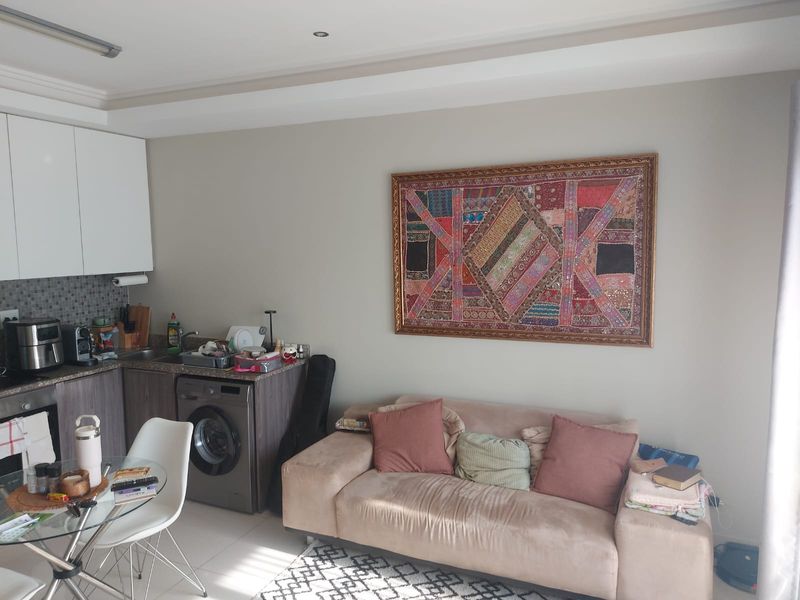 Open-plan living area featuring a compact kitchen with built-in cabinetry, granite countertops, and an integrated washing machine, seamlessly connected to the lounge space.