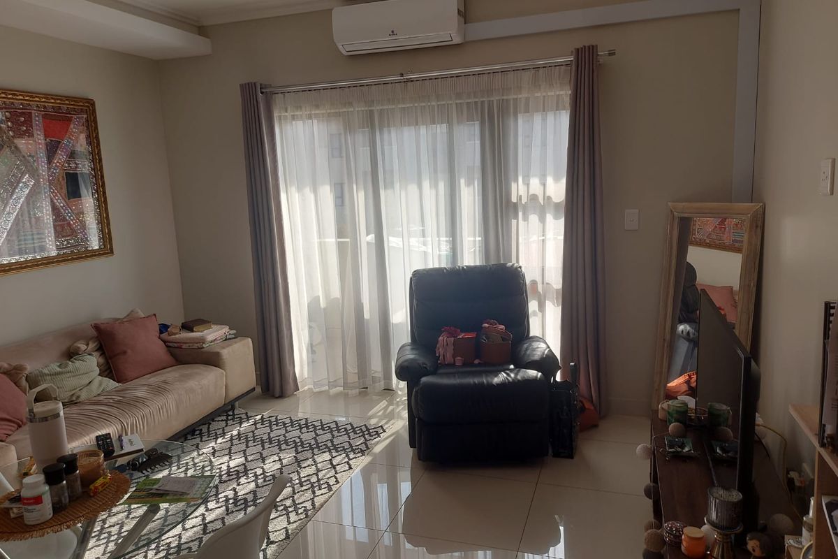 A bright living room featuring polished tiled flooring, a wall-mounted split-system air conditioner, and large sliding glass doors leading to an outdoor area.
