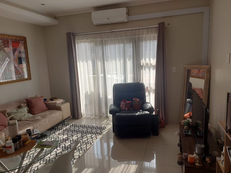 A bright living room featuring polished tiled flooring, a wall-mounted split-system air conditioner, and large sliding glass doors leading to an outdoor area.