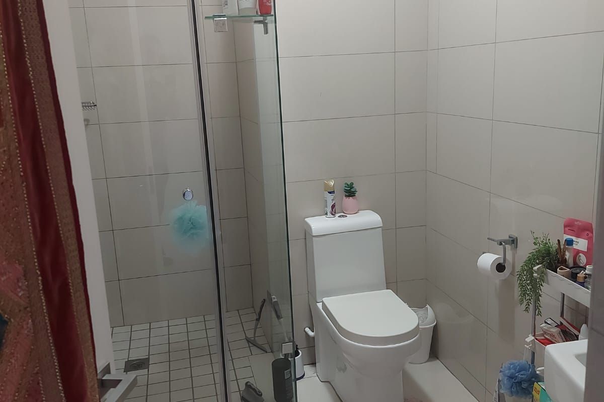 A functional bathroom featuring a glass-enclosed shower, modern toilet, and neutral wall and floor tiling throughout.