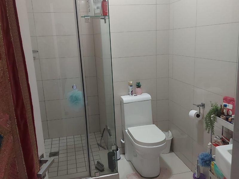 A functional bathroom featuring a glass-enclosed shower, modern toilet, and neutral wall and floor tiling throughout.