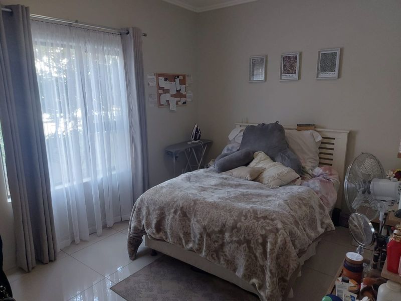 A functional bedroom featuring tiled flooring and a large window with curtain treatments, providing natural light to the space.