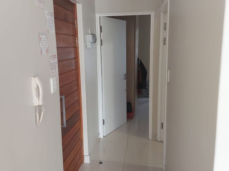 A clean, neutral-toned hallway featuring tiled flooring, a timber entrance door, and an integrated intercom system.