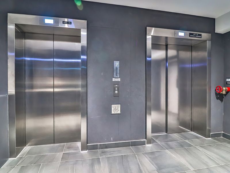 A modern apartment building elevator lobby featuring dual stainless steel lift doors, tiled flooring, and a fire safety valve.
