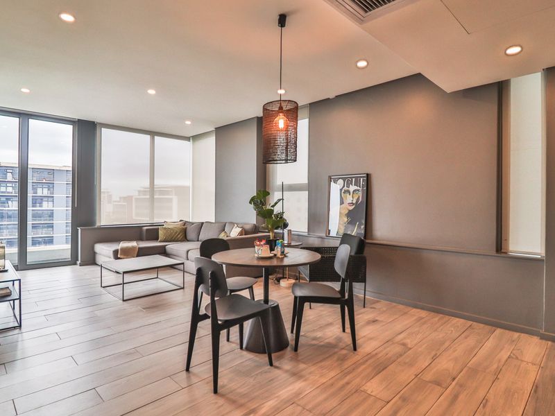 Modern open-plan living and dining area featuring timber-look flooring, recessed lighting, and expansive floor-to-ceiling windows with city views.