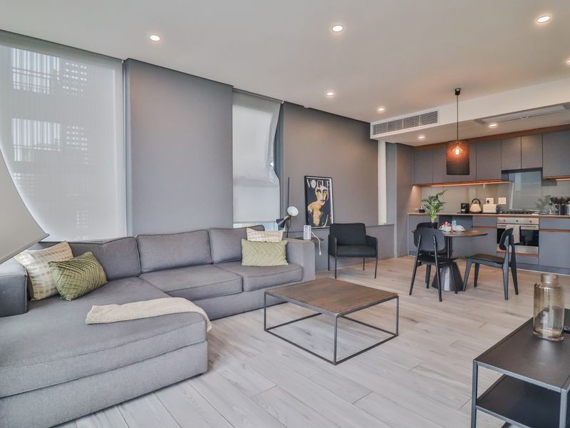 Modern open-plan living area featuring a sleek kitchen with built-in appliances, recessed lighting, ducted air conditioning, and light timber-look flooring.