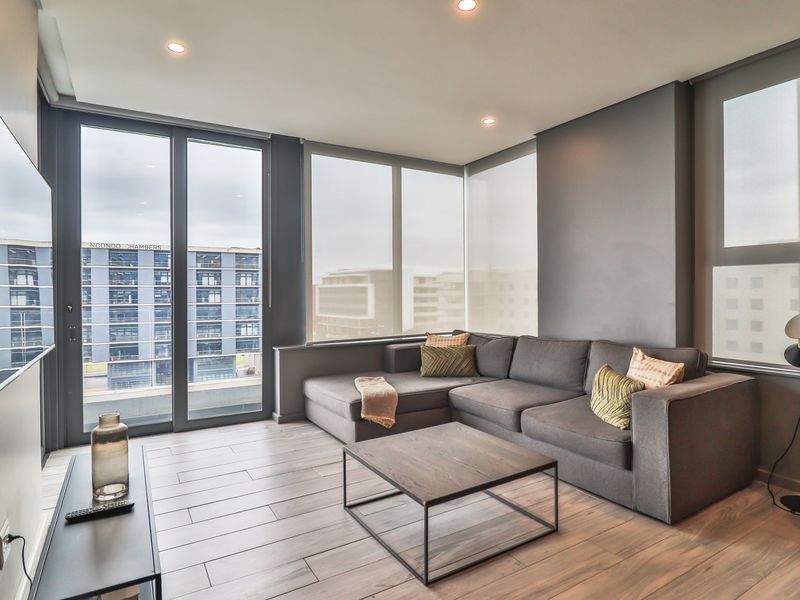 Modern living room featuring large floor-to-ceiling windows, sleek floor tiles, recessed lighting, and direct access to an outdoor area.