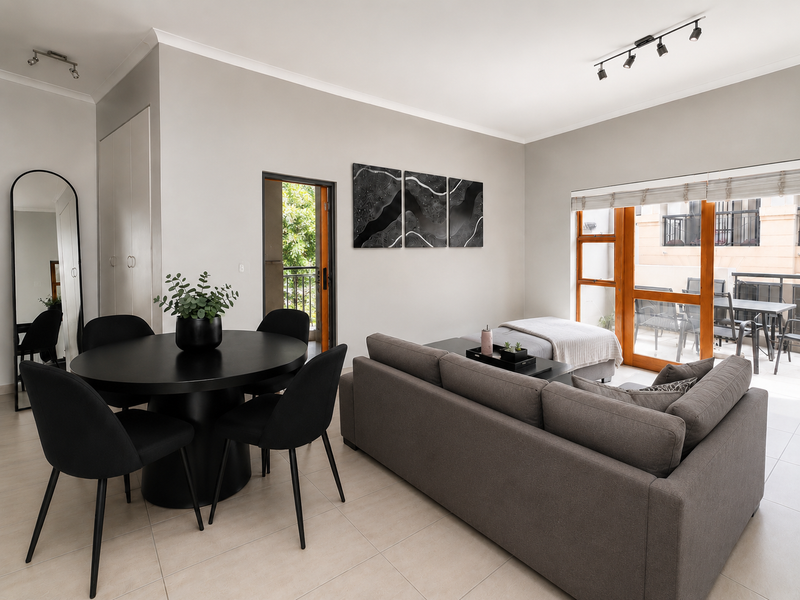 A bright open-plan living and dining area featuring neutral tiled flooring, modern track lighting, and direct access to an outdoor balcony through sliding glass doors.