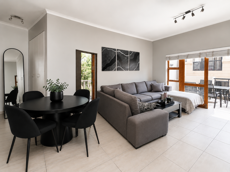 Bright open-plan living and dining area featuring neutral tiled flooring, modern track lighting, and direct access to an outdoor balcony through sliding glass doors.