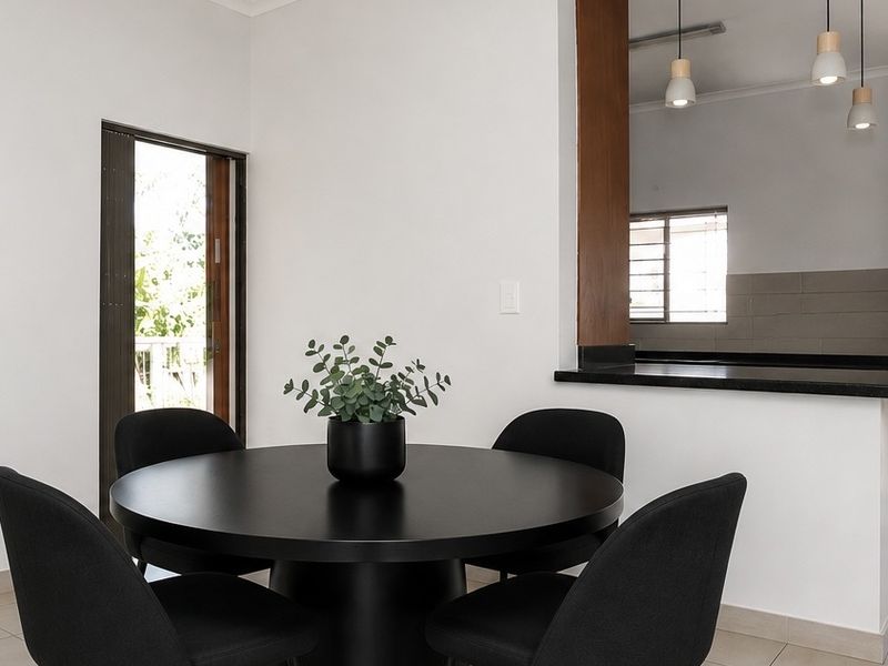 An open-plan dining area featuring modern pendant lighting, tiled flooring, and a breakfast bar overlooking the kitchen, with access to an outdoor space.