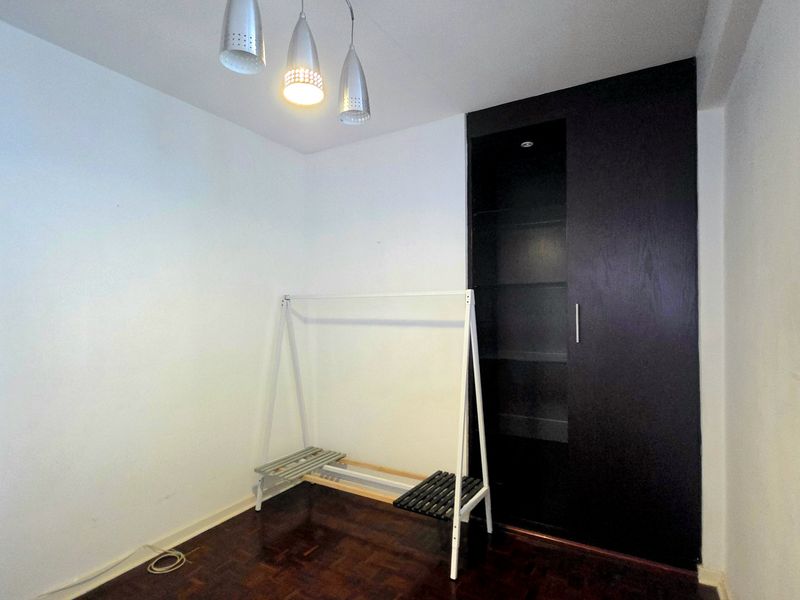 A bedroom featuring dark wood parquet flooring, a built-in wardrobe, and venetian blinds, offering a clean and functional space.