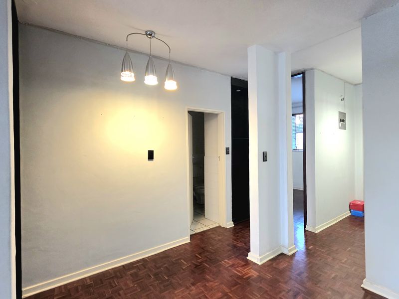 A vacant hallway featuring classic parquet flooring and a central pendant light fixture, providing access to adjacent rooms within the apartment.