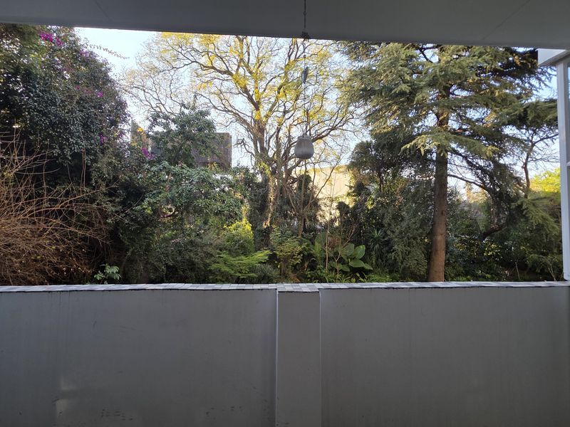 A covered balcony area featuring a solid tiled balustrade and views of mature trees and garden greenery.