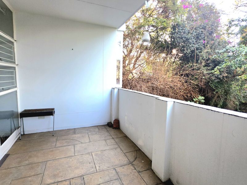 A covered balcony featuring tiled flooring and a masonry balustrade, offering a private outdoor space with views of surrounding greenery.