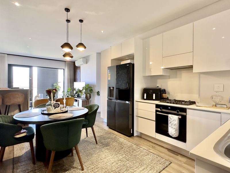 Modern open-plan kitchen and dining area featuring sleek white cabinetry, integrated appliances, recessed lighting, and direct access to a balcony.