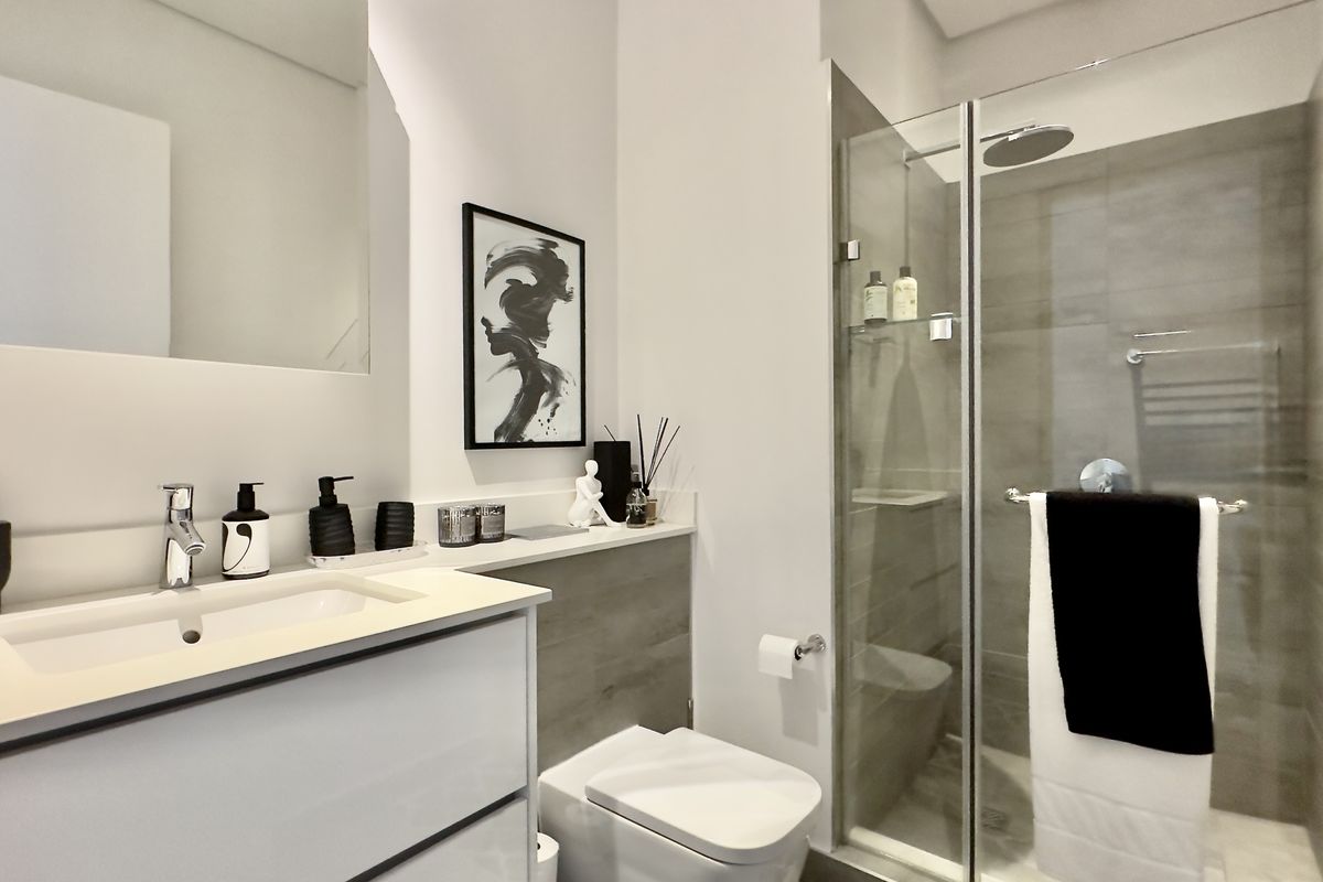 Modern bathroom featuring a sleek vanity, glass-enclosed shower with rain shower head, wall-mounted mirror, and a heated towel rail.