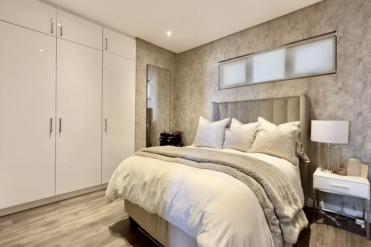 A well-maintained bedroom featuring modern built-in wardrobes, laminate flooring, and neutral textured wallpaper, providing a clean and contemporary living space.