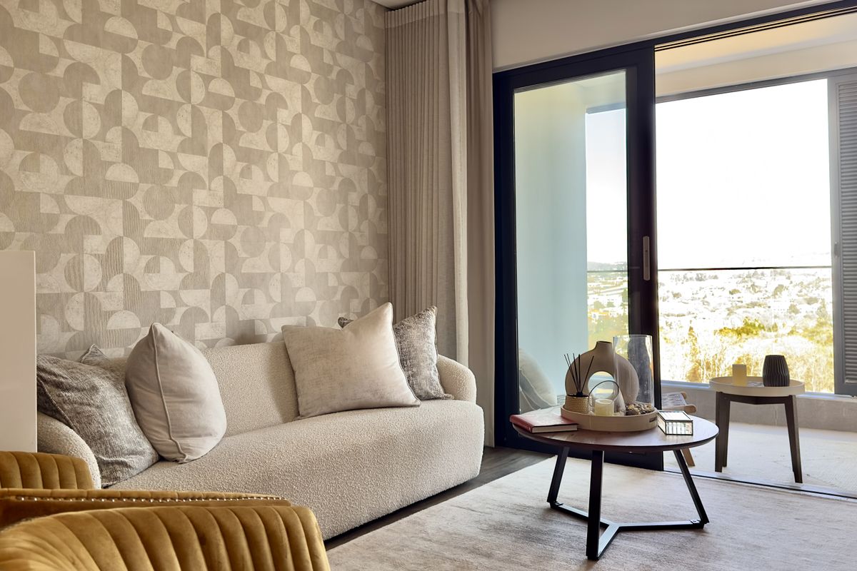 A well-lit living room featuring patterned wallpaper and a large sliding glass door providing access to a balcony with scenic views.