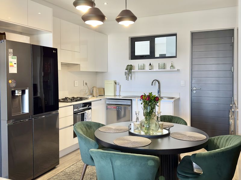 Modern open-plan kitchen and dining area featuring sleek white cabinetry, integrated appliances, gas hob, and contemporary pendant lighting.