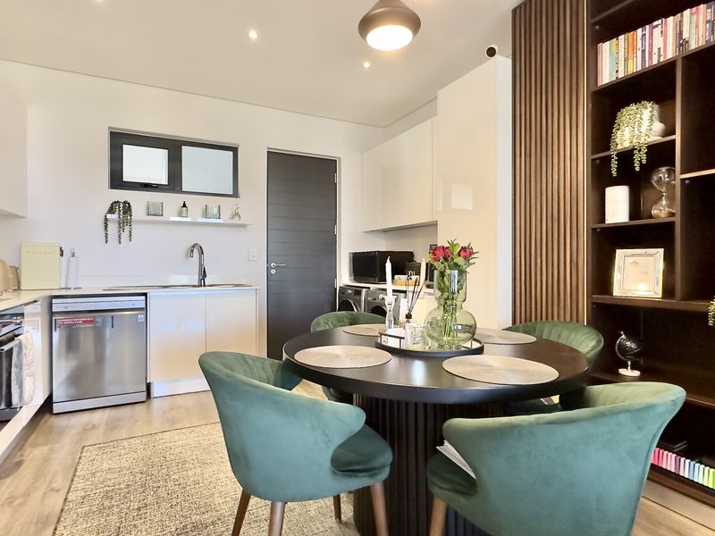 Modern open-plan kitchen and dining area featuring sleek cabinetry, integrated appliances, a stylish slatted wood feature wall, and built-in shelving.