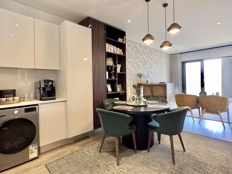 Modern open-plan living area featuring sleek built-in cabinetry, integrated laundry appliances, contemporary pendant lighting, and seamless access to an outdoor balcony.