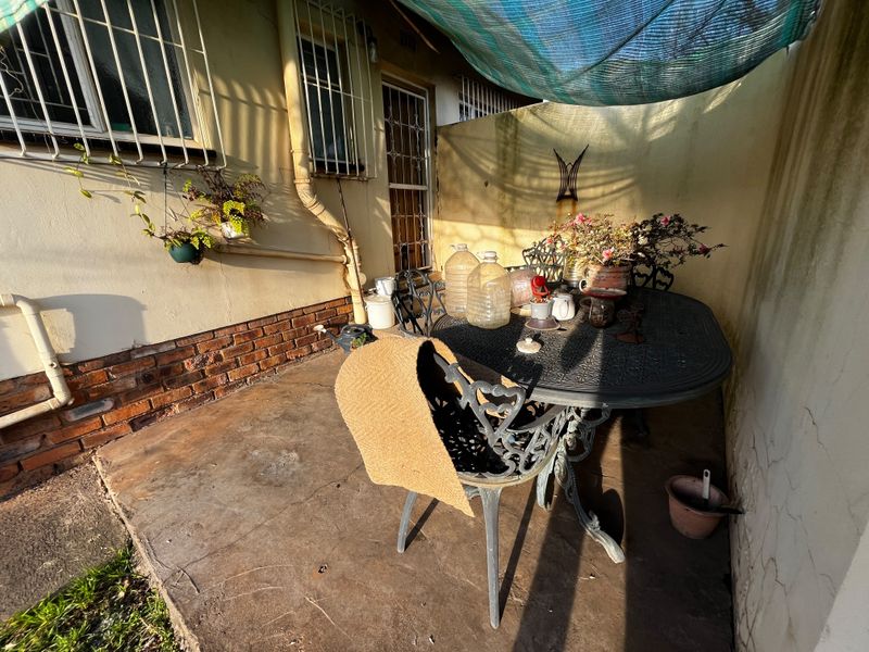 A small outdoor patio area featuring a brick base wall, security bars on windows, and a shade cloth covering, showing signs of wear.