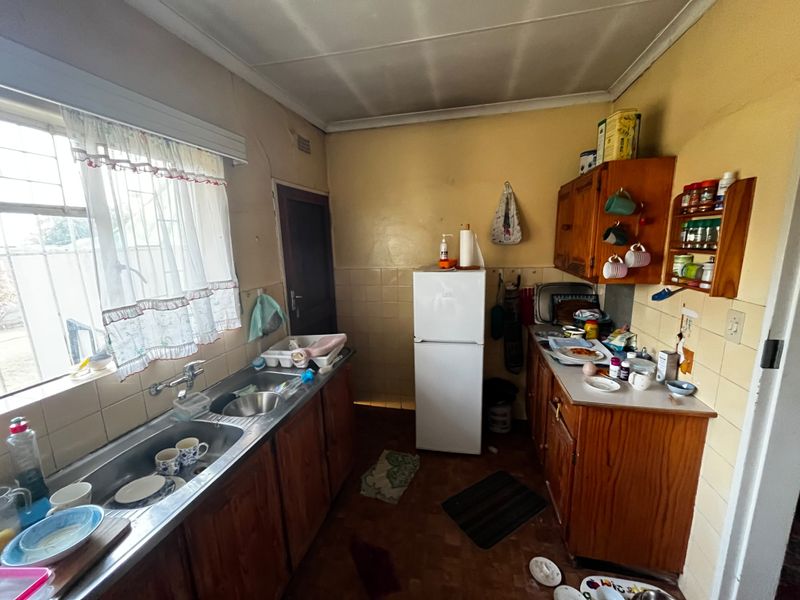 A dated kitchen featuring wooden cabinetry, a double stainless steel sink, and tiled splashbacks, offering significant potential for modernization and renovation.