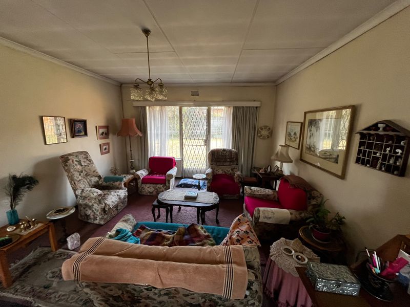 A dated living room featuring a chandelier, carpet flooring, and a security gate leading to the exterior.