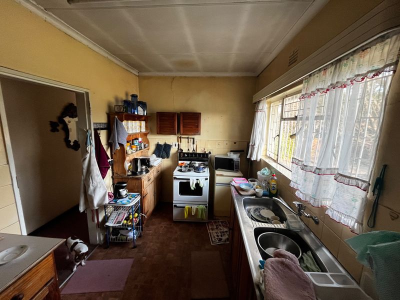 A dated kitchen featuring a double bowl stainless steel sink, freestanding stove, and tiled splashback, requiring cosmetic updates and repairs to wall finishes.