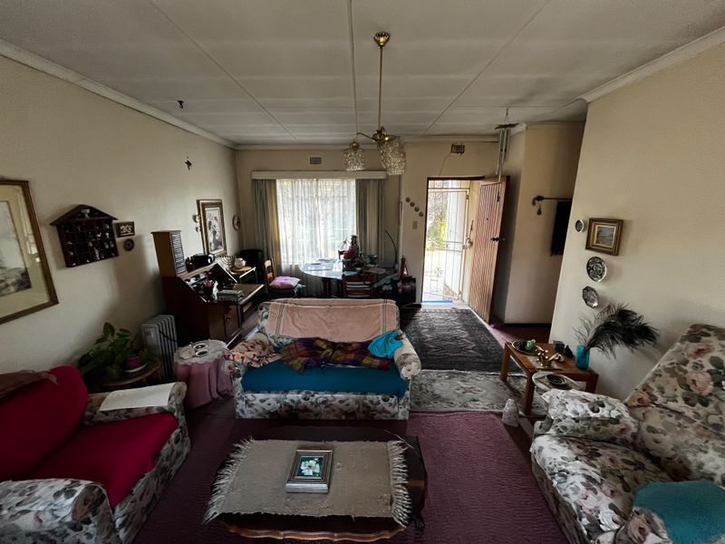 A dated living room featuring a tiled ceiling, direct access to the exterior via a security gate, and large windows allowing natural light.