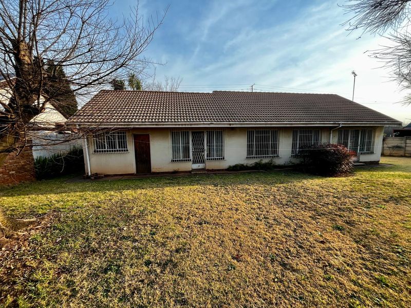 Rear view of a single-story house featuring a tiled roof, security bars on windows, and a large backyard area.
