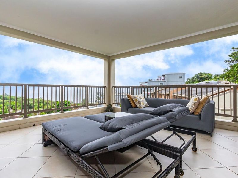 Spacious covered balcony featuring tiled flooring and a metal balustrade, offering an open-air outdoor living space with scenic views.