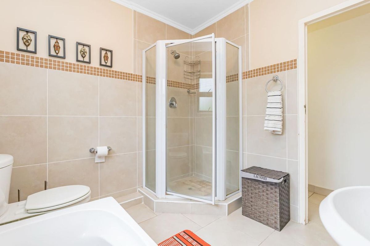 A functional bathroom featuring a corner shower enclosure, a bathtub, and neutral wall tiling with a decorative mosaic border.