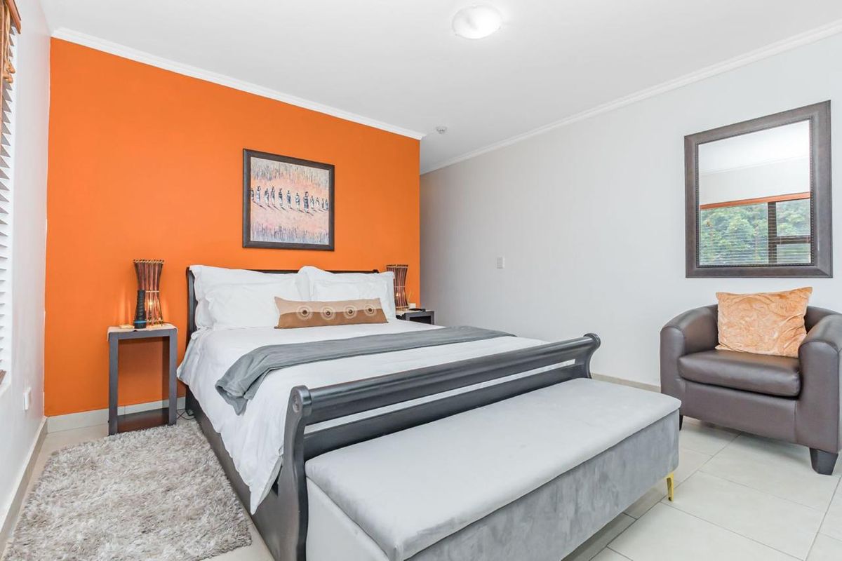 A bedroom featuring tiled flooring, a bright orange accent wall, and a window with fitted blinds.
