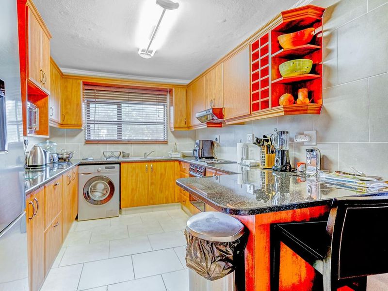 A functional kitchen featuring wooden cabinetry, granite countertops, integrated laundry appliances, and a breakfast bar area with tiled finishes.