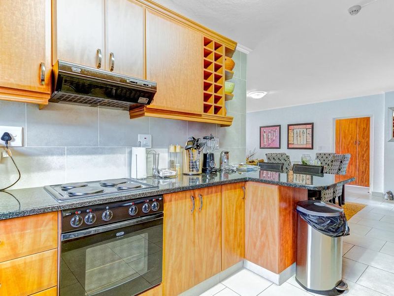 A functional kitchen featuring wooden cabinetry, granite countertops, a built-in oven, and an electric hob, with an open-plan layout leading to the dining area.
