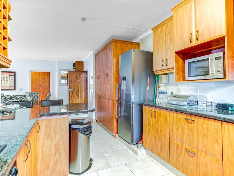 A functional kitchen featuring wooden cabinetry, granite countertops, built-in microwave, and tiled flooring, offering a practical layout for daily use.