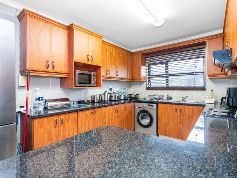 A functional kitchen featuring wooden cabinetry, granite countertops, a built-in microwave, and an integrated washing machine with a tiled backsplash.