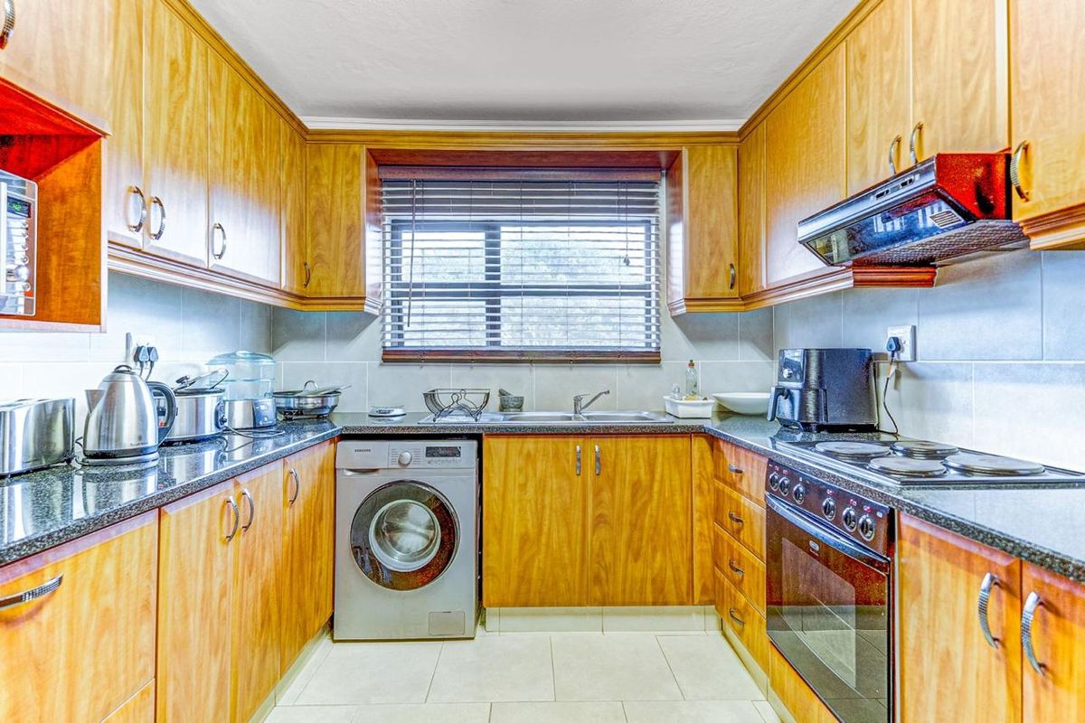 A functional galley-style kitchen featuring wooden cabinetry, granite countertops, integrated oven and hob, and a dedicated space for a washing machine.