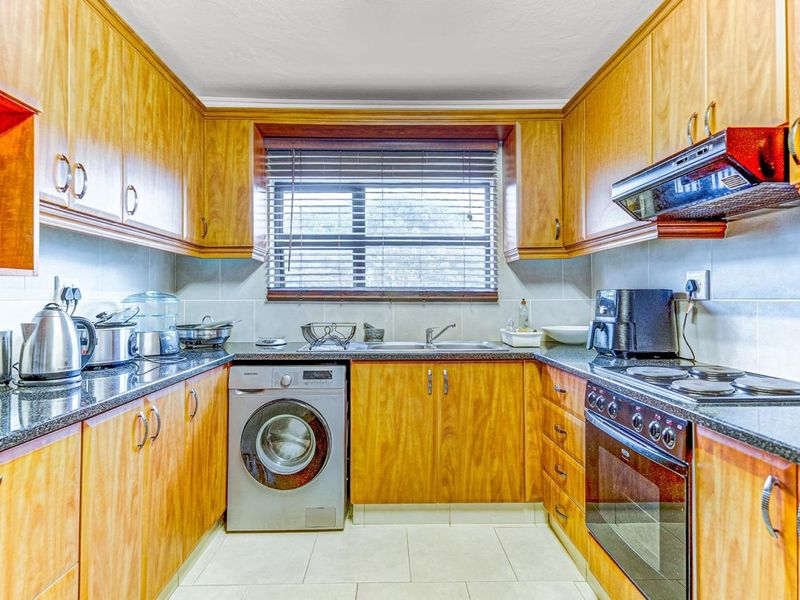A functional galley-style kitchen featuring wooden cabinetry, granite countertops, integrated oven and hob, and a dedicated space for a washing machine.