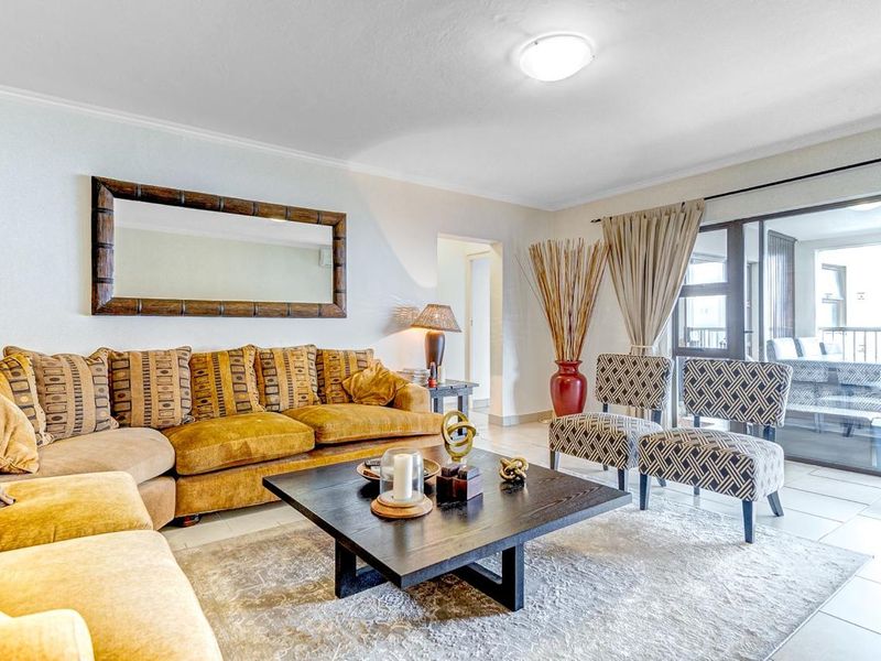 A bright and spacious living room featuring tiled flooring and a large sliding glass door providing access to the balcony.